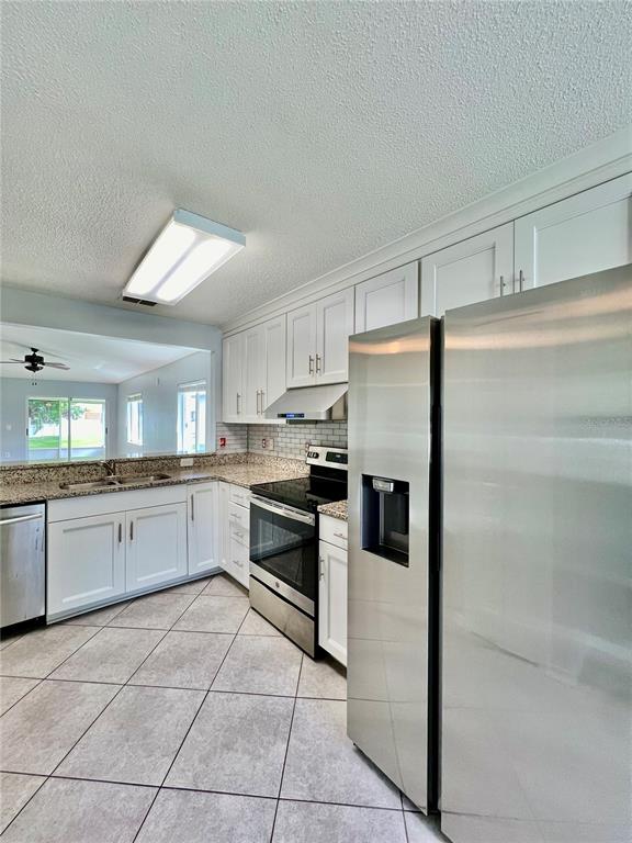 A kitchen features white cabinets, stainless steel appliances, granite countertops, and light-colored tile flooring — 27147 BIG SUR DRIVE, WESLEY CHAPEL, FL
