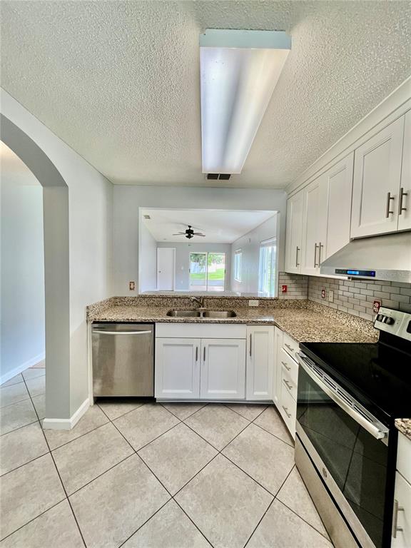 A kitchen features white cabinets, granite countertops, stainless steel appliances, and tile flooring — 27147 BIG SUR DRIVE, WESLEY CHAPEL, FL