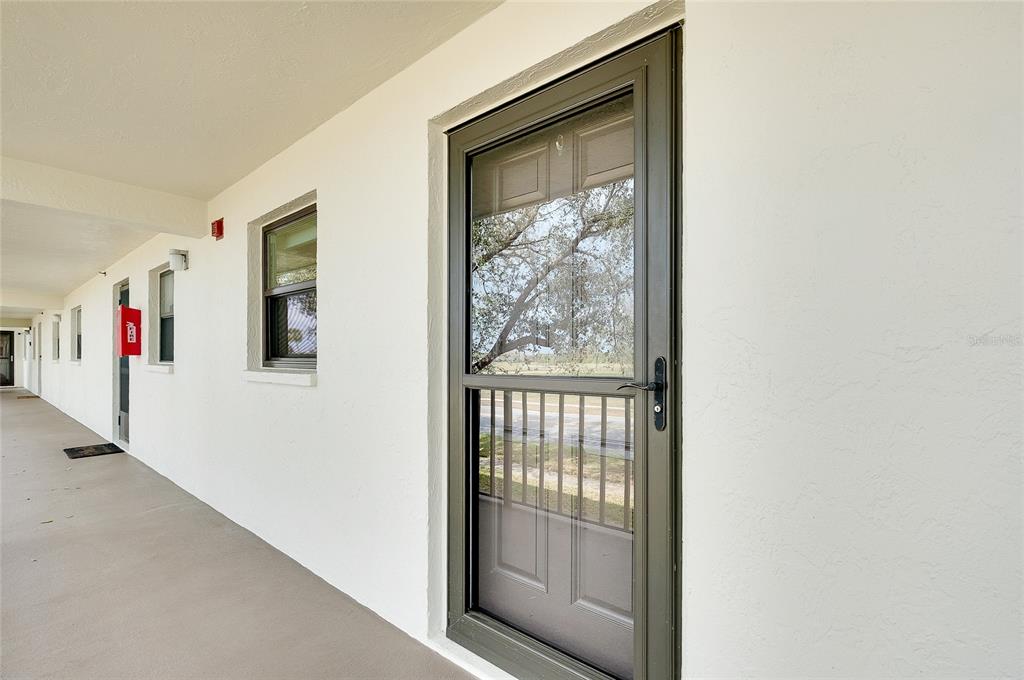 A view of a covered exterior walkway with a dark-framed storm door and windows — 104 CAPRI ISLES BOULEVARD UNIT 209, VENICE, FL