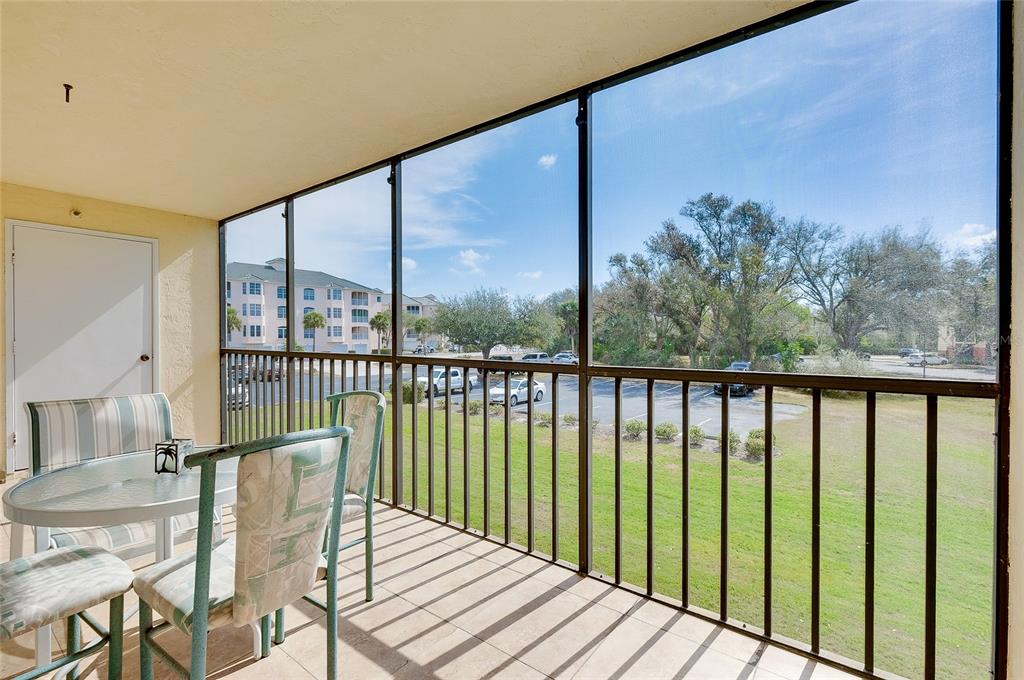 A screened-in balcony features patio furniture and views of a parking lot and trees — 104 CAPRI ISLES BOULEVARD UNIT 209, VENICE, FL
