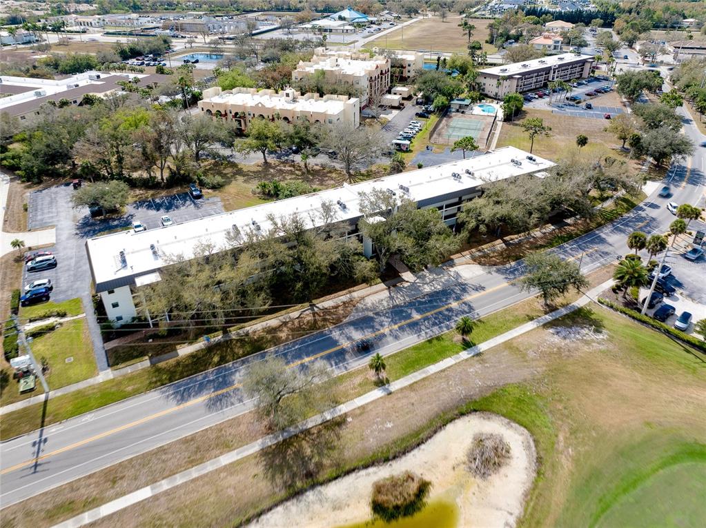 An aerial view shows a long, multi-story apartment building with a white roof near a road — 104 CAPRI ISLES BOULEVARD UNIT 209, VENICE, FL
