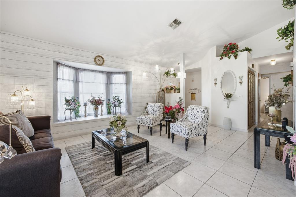 A living room features white shiplap walls, a bay window, tile flooring, and floral armchairs — 549 SILVER COURSE RUN, OCALA, FL