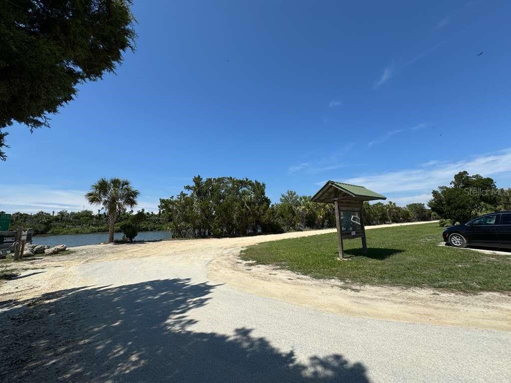 A gravel path leads toward a waterfront area with a wooden information kiosk and trees — 11624 N LANDOVER TERRACE, DUNNELLON, FL