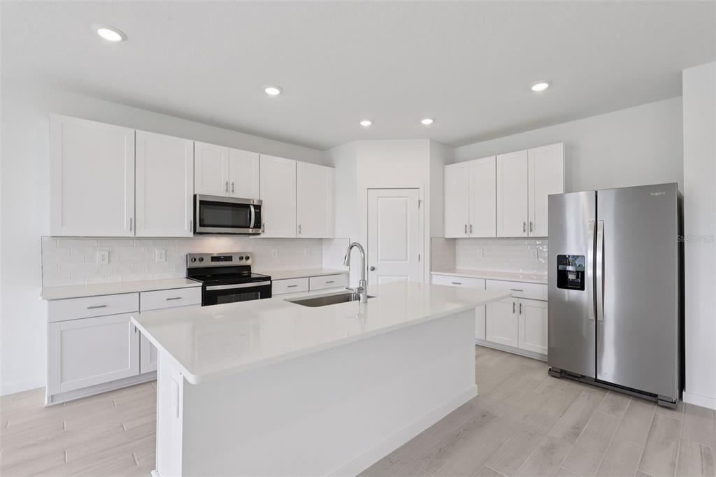 A modern kitchen features white cabinets, stainless steel appliances, a center island, and light flooring — 76 ARARAT DRIVE, PALM COAST, FL