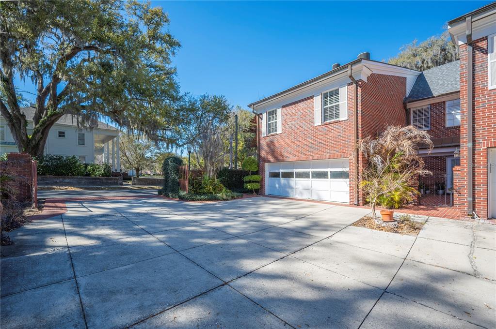 A brick house features a white garage door and a concrete driveway under large trees — 155 LAKE MORTON DRIVE UNIT 1, LAKELAND, FL