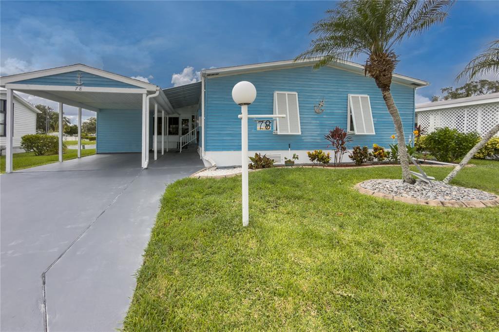 A light blue mobile home features a carport, a front lawn, and a palm tree — 78 EAGLE CIRCLE, ELLENTON, FL