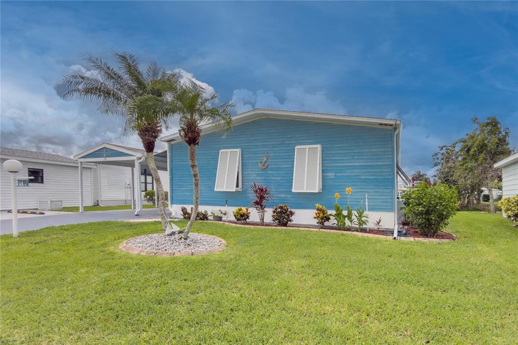 A blue mobile home with a palm tree and a carport sits on a grassy lawn — 78 EAGLE CIRCLE, ELLENTON, FL