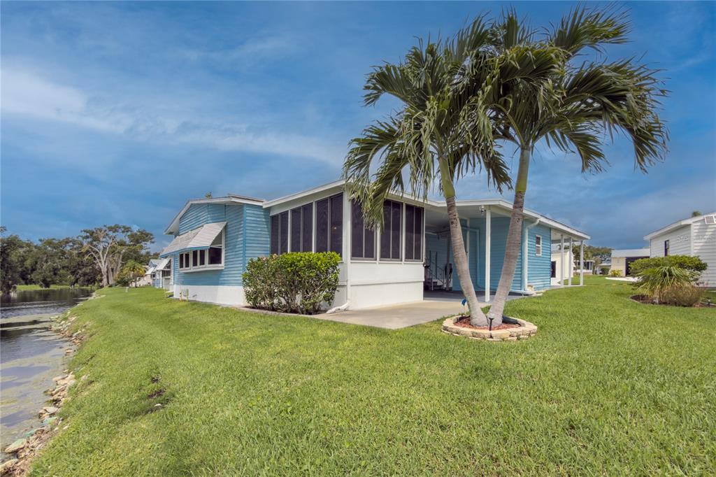 A blue mobile home with a screened-in porch sits on a grassy lot beside water — 78 EAGLE CIRCLE, ELLENTON, FL