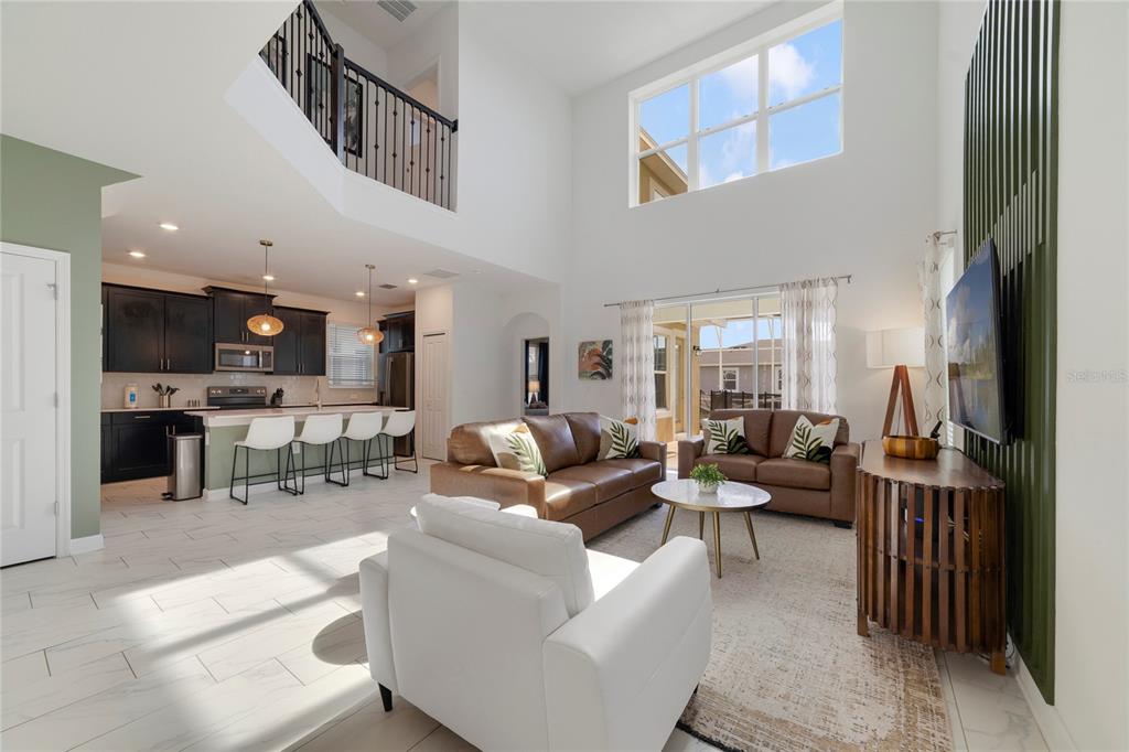 A bright, open-concept living room and kitchen featuring high ceilings, tile floors, and brown furniture — 9199 SOMMERSET HILLS DRIVE, DAVENPORT, FL