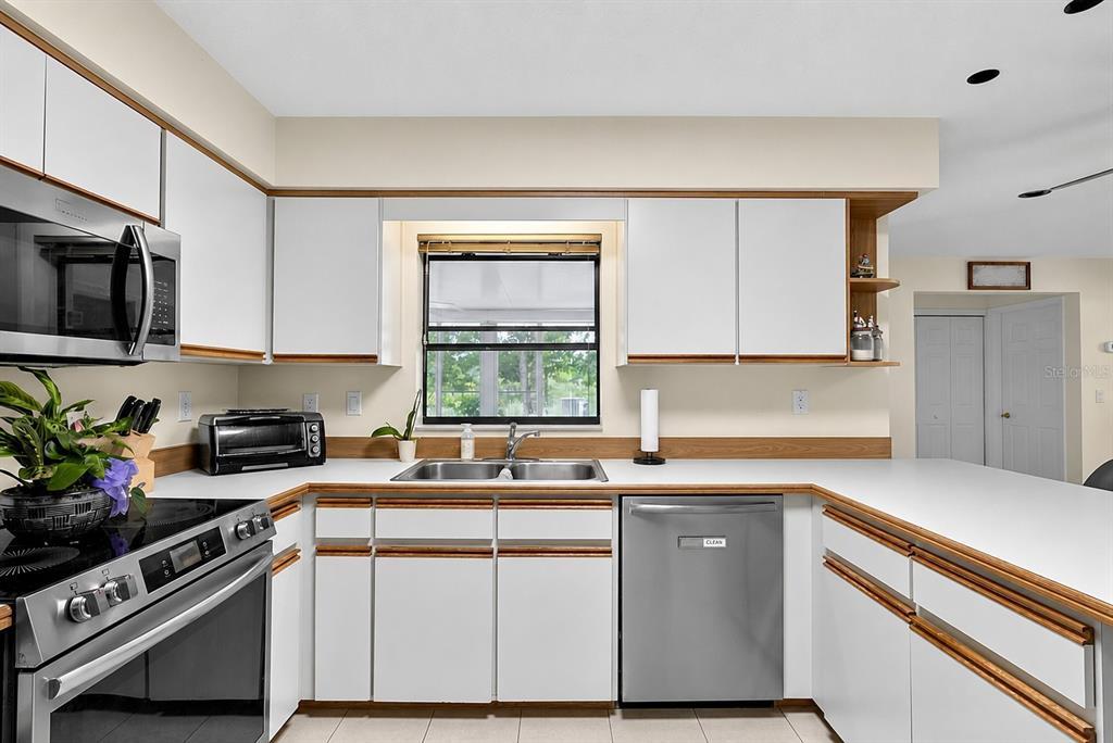 A kitchen features white cabinets with wood trim, stainless steel appliances, and a double sink — 1408 ROYAL GROVE LANE, PORT ORANGE, FL