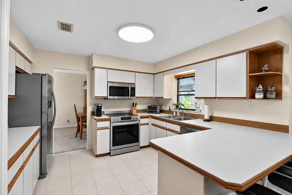 A kitchen features white cabinets, stainless steel appliances, and a peninsula with a white countertop — 1408 ROYAL GROVE LANE, PORT ORANGE, FL