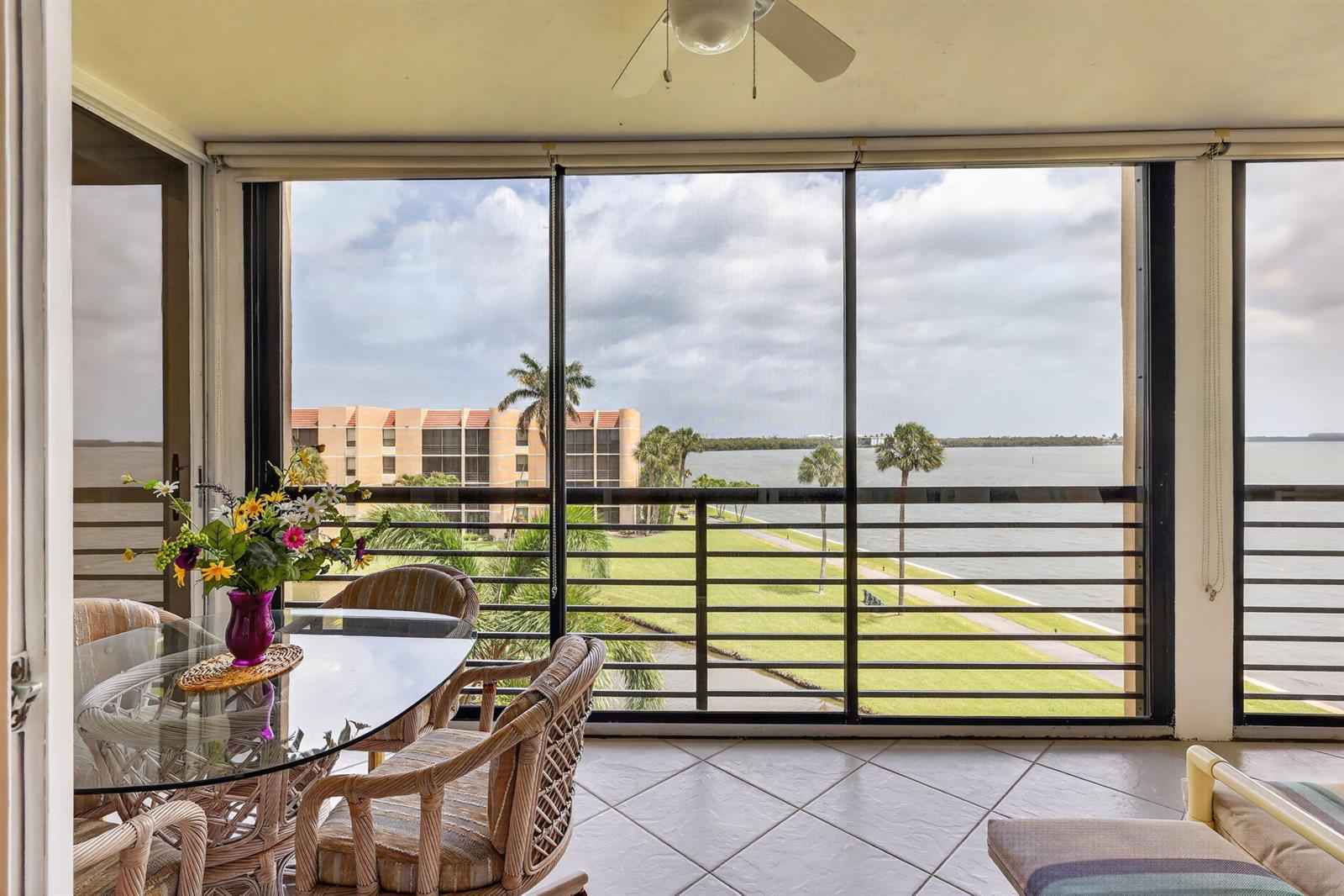 A screened-in balcony features a glass dining table, wicker chairs, and a waterfront view — 3382 NE Causeway Boulevard # 403, Jensen Beach FL 34957, JENSEN BEACH, FL