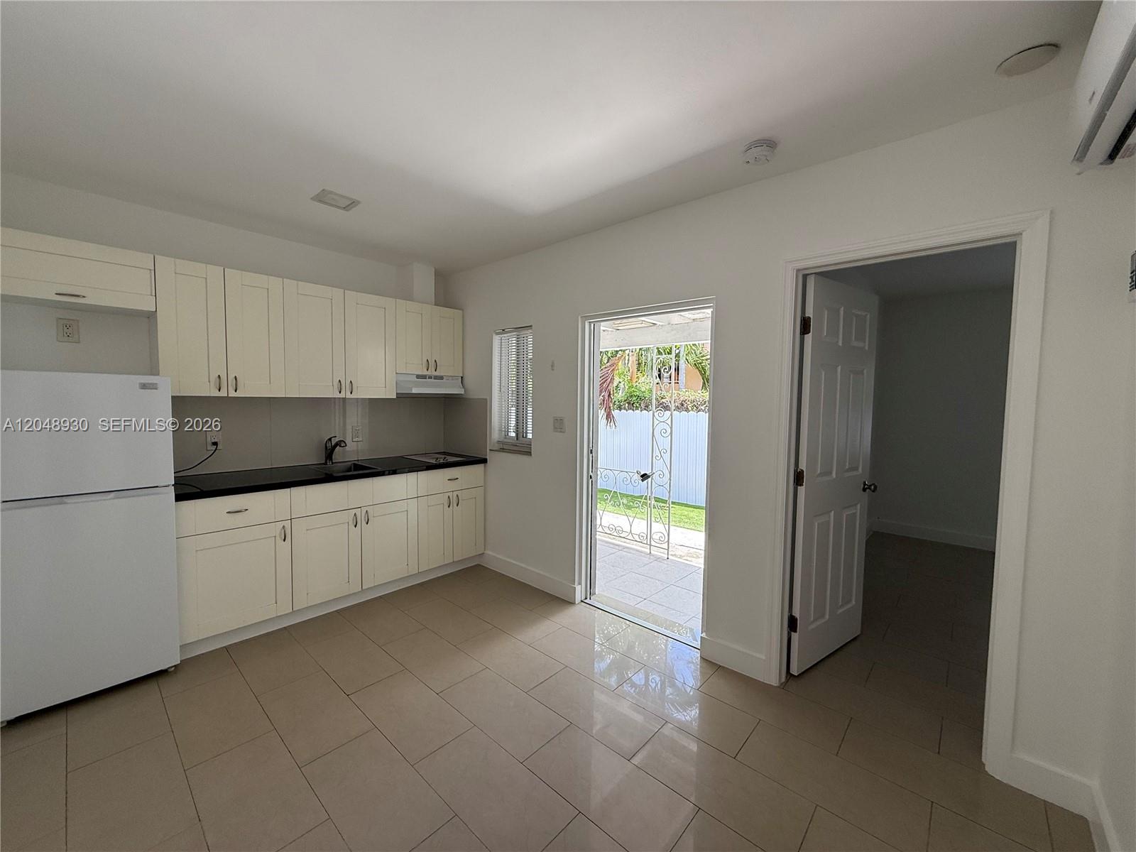A kitchen with white cabinets, black countertops, and tile flooring leads to an outdoor patio — 242 NE 55th Ter # 2, Miami FL 33137, MIAMI, FL