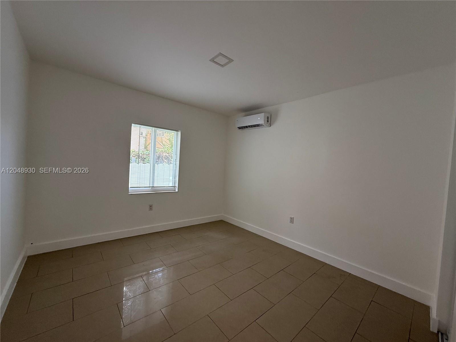 An empty room features white walls, tile flooring, a window, and a wall-mounted air conditioner — 242 NE 55th Ter # 2, Miami FL 33137, MIAMI, FL