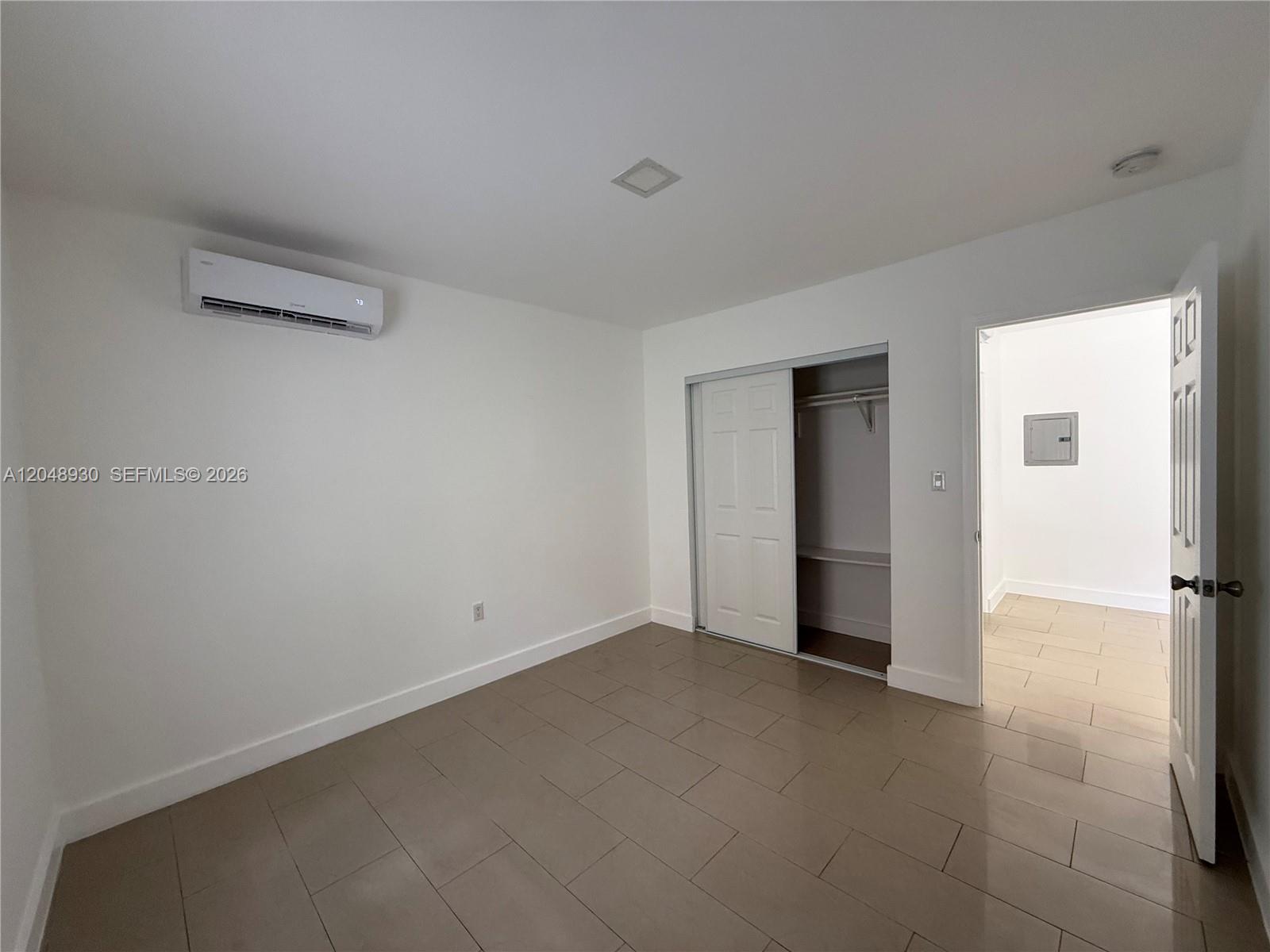 An empty bedroom features white walls, tile flooring, a sliding closet, and a wall-mounted AC unit — 242 NE 55th Ter # 2, Miami FL 33137, MIAMI, FL