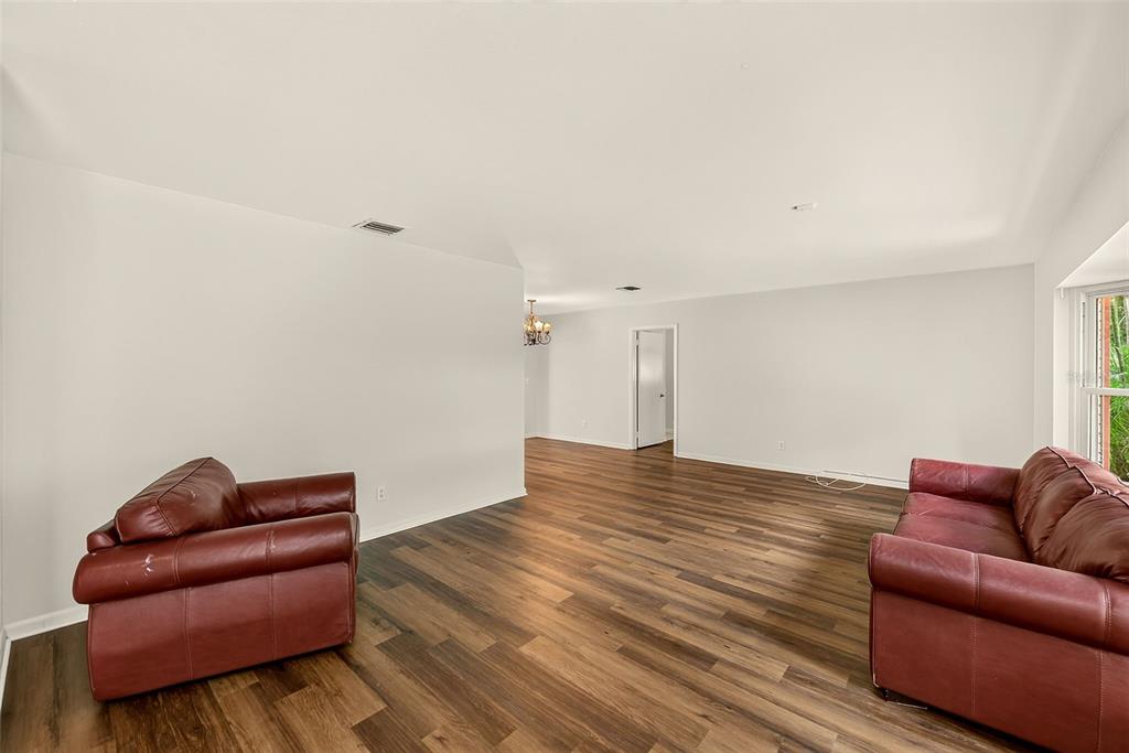 A living room with wood-look flooring, white walls, and two red leather sofas — 303 SAINT AUGUSTINE AVENUE, TEMPLE TERRACE, FL