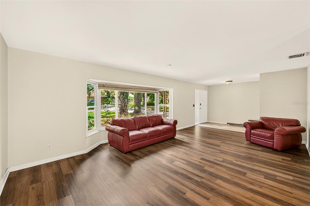 A living room with wood-look flooring, a large bay window, and two red leather sofas — 303 SAINT AUGUSTINE AVENUE, TEMPLE TERRACE, FL