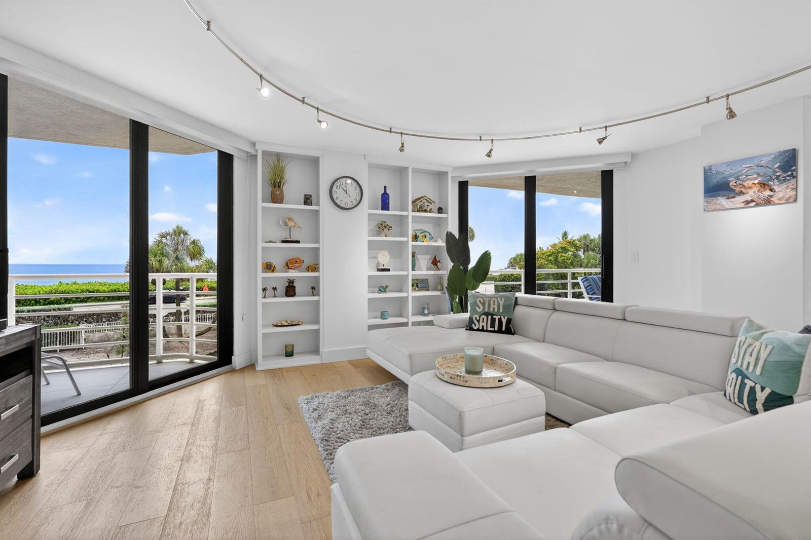 A bright living room features a white sectional sofa, built-in shelving, and floor-to-ceiling windows — 176 Helios Drive # 205, Jupiter FL 33477, JUPITER, FL