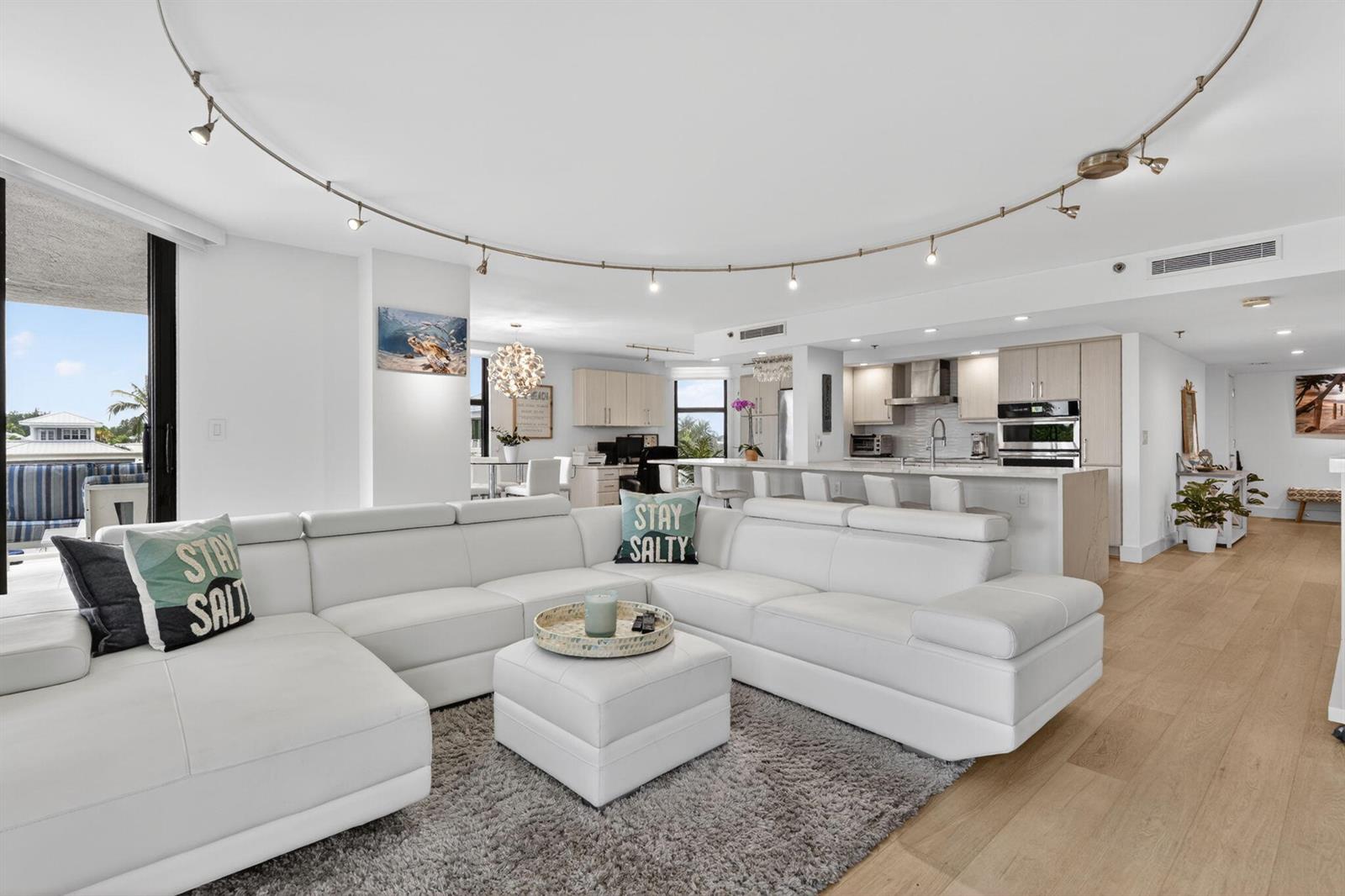 A modern open-concept living room features a white sectional sofa, kitchen, and light wood flooring — 176 Helios Drive # 205, Jupiter FL 33477, JUPITER, FL