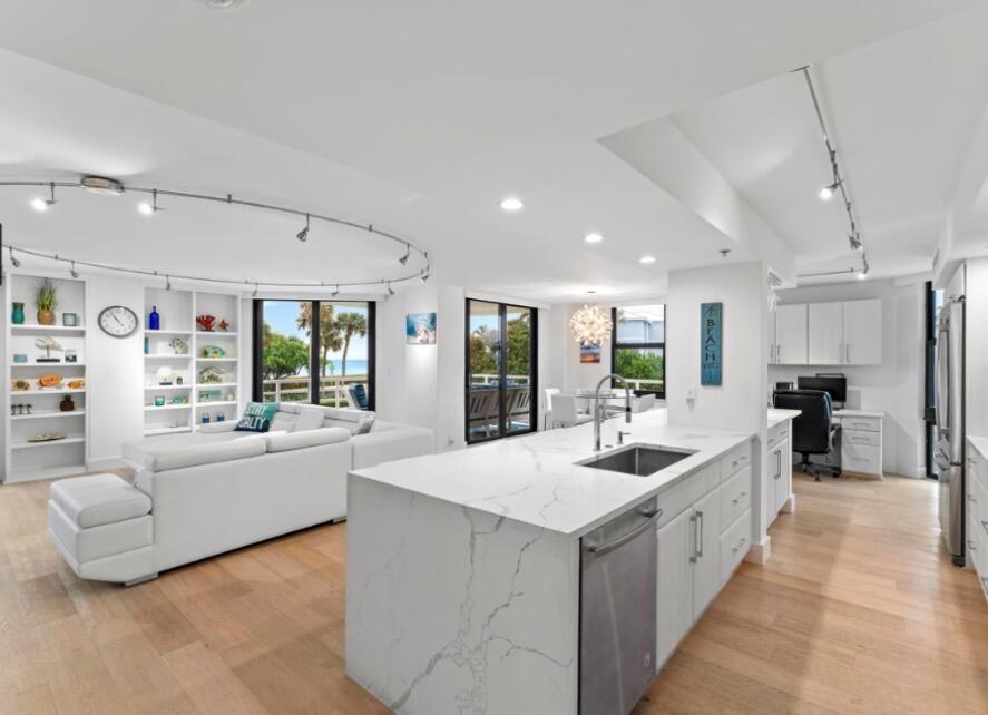 A bright, open-concept kitchen and living area featuring white cabinetry, marble countertops, and hardwood floors — 176 Helios Drive # 205, Jupiter FL 33477, JUPITER, FL