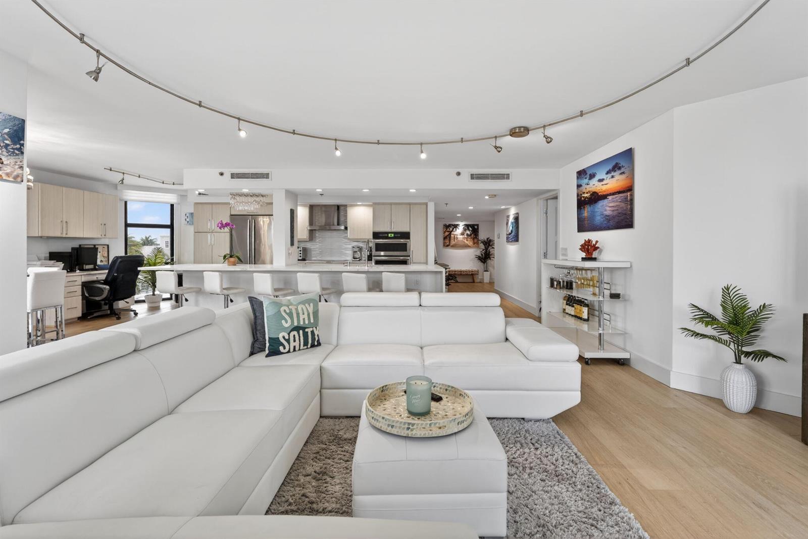 A modern open-concept living room features a white sectional sofa, kitchen island, and track lighting — 176 Helios Drive # 205, Jupiter FL 33477, JUPITER, FL