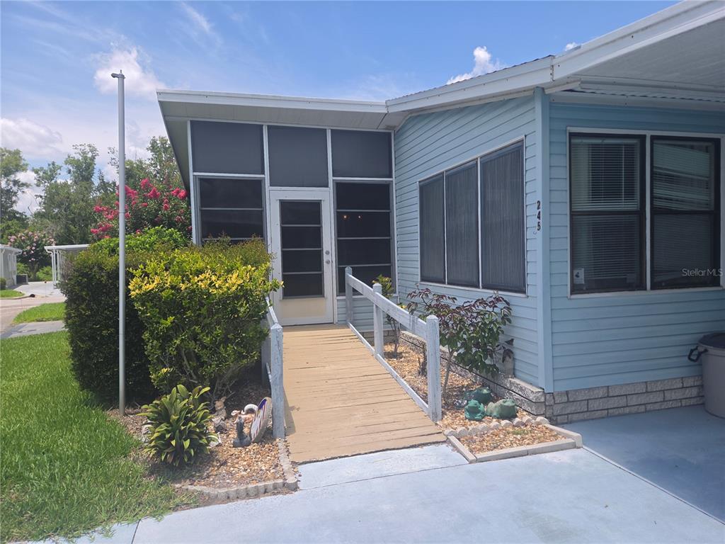 A light blue mobile home features a wooden wheelchair ramp leading to a screened-in porch — 245 RAMSGATE WAY, HAINES CITY, FL
