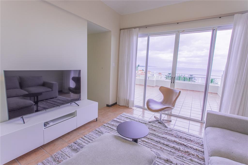 A living room features a television, modern furniture, and a balcony overlooking the ocean — 115 CARRETERA 115, KM. 5.8 UNIT 603-A, ANASCO, PR