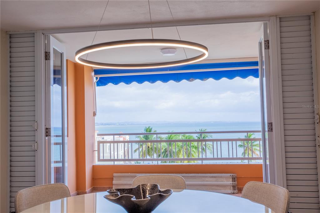 A dining area with a modern circular light fixture opens onto a balcony overlooking the ocean — 115 CARRETERA 115, KM. 5.8 UNIT 603-A, ANASCO, PR
