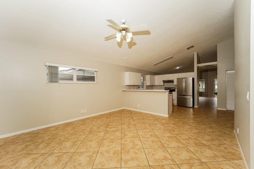 An open-concept living area features beige tile flooring, a ceiling fan, and a kitchen pass-through — COCONUT CREEK, FL