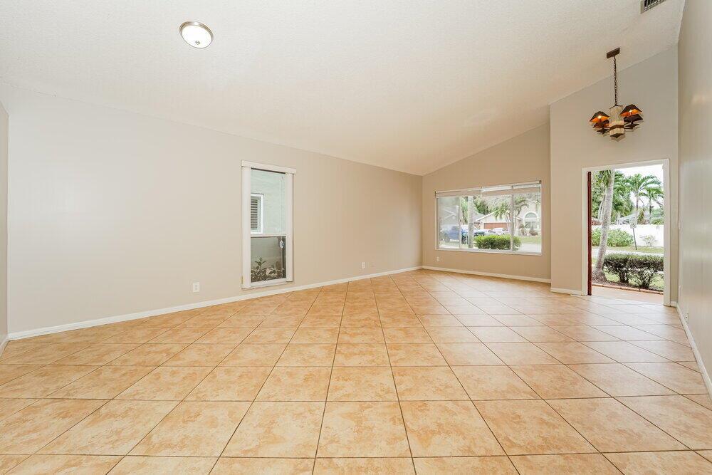 An empty living room features light-colored walls, tan tile flooring, and a vaulted ceiling — COCONUT CREEK, FL