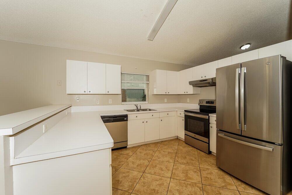A kitchen with white cabinets, stainless steel appliances, and tan tile flooring — COCONUT CREEK, FL