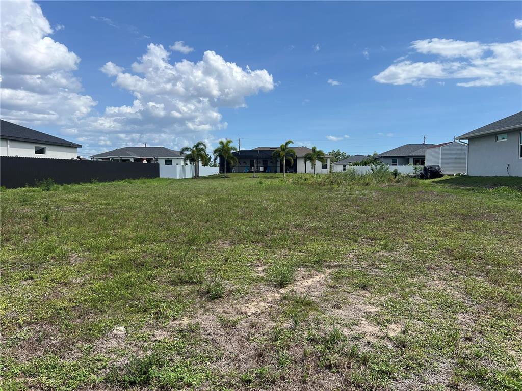A vacant, grassy residential lot is surrounded by neighboring houses and palm trees — 406 JACARANDA PKWY E, CAPE CORAL, FL