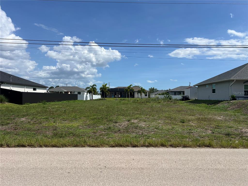 A vacant residential lot sits between two houses under a blue sky with clouds — 406 JACARANDA PKWY E, CAPE CORAL, FL