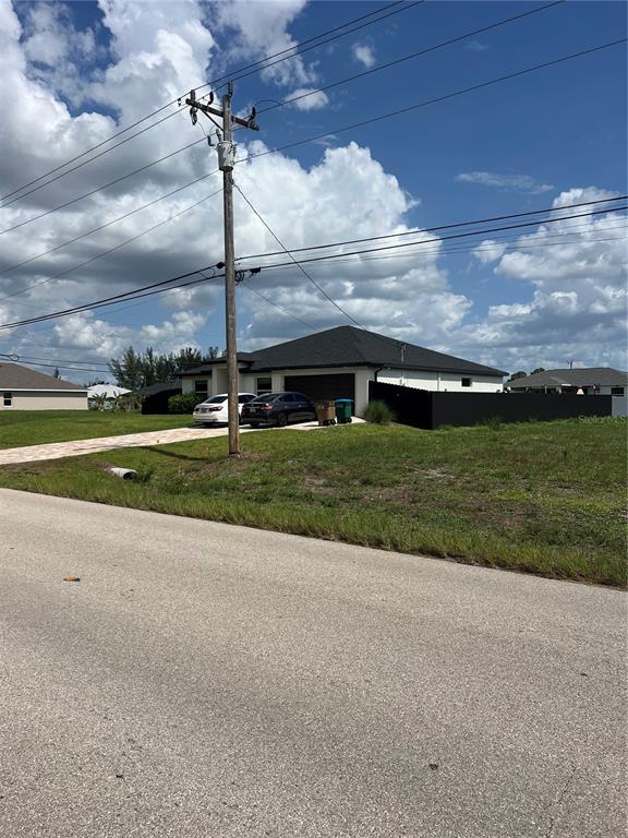 A single-story house with a black roof and fence sits behind a utility pole — 406 JACARANDA PKWY E, CAPE CORAL, FL