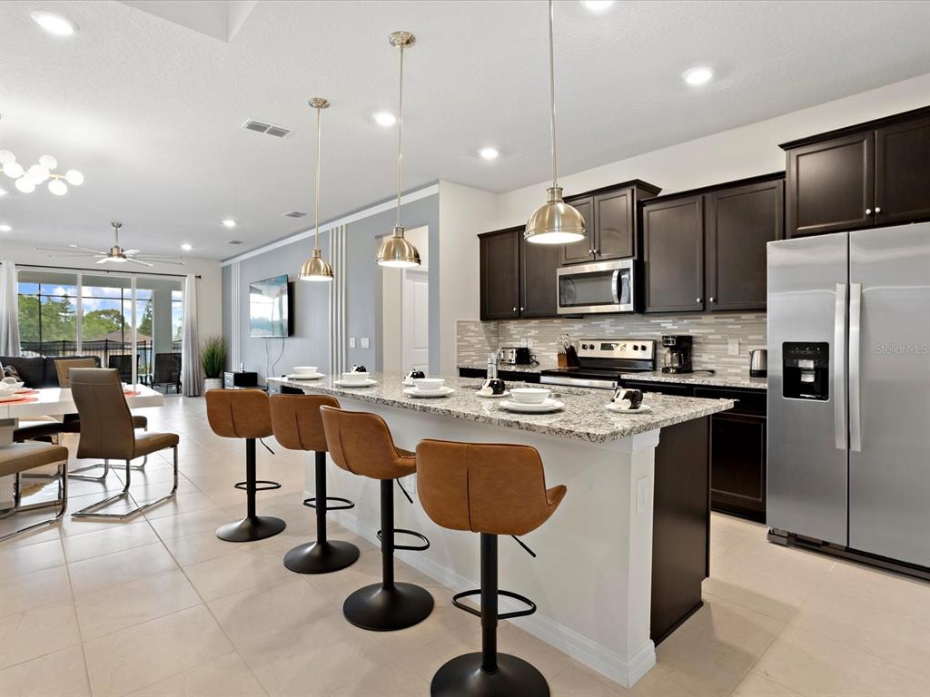 A kitchen with dark cabinets, granite countertops, and a breakfast bar with four stools — 3835 LANA AVENUE, DAVENPORT, FL