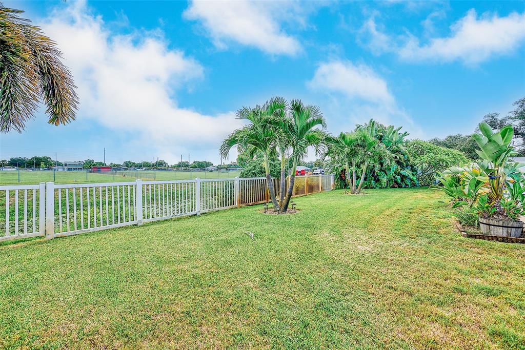 A grassy backyard features a white fence, several palm trees, and a blue sky — 9069 127TH STREET, SEMINOLE, FL
