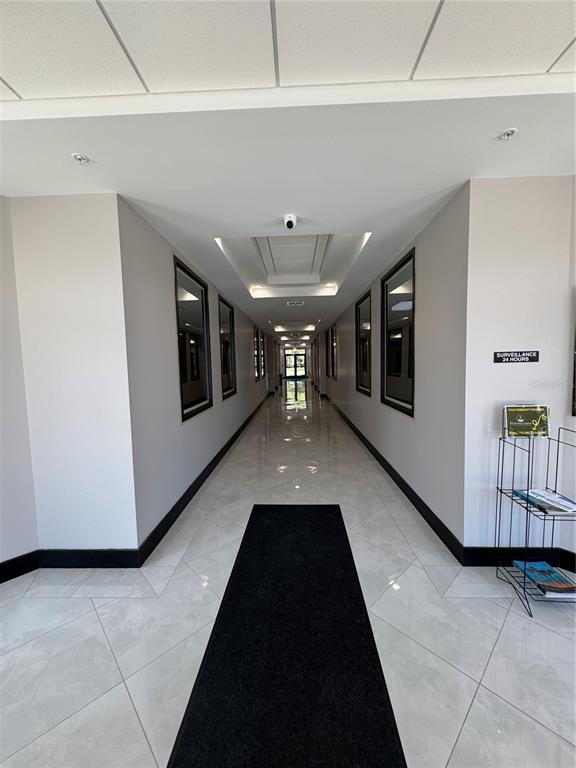 A long, brightly lit hallway features light-colored tile flooring, a black runner rug, and recessed lighting — 13564 VILLAGE PARK DRIVE UNIT 310, ORLANDO, FL