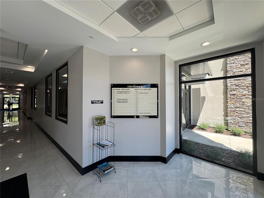 A bright office building lobby features a directory sign, tile flooring, and glass exterior doors — 13564 VILLAGE PARK DRIVE UNIT 310, ORLANDO, FL