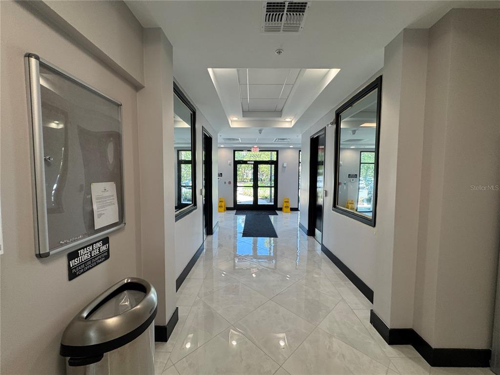 A brightly lit hallway features polished tile floors, framed mirrors, and a glass-paned exit door — 13564 VILLAGE PARK DRIVE UNIT 310, ORLANDO, FL