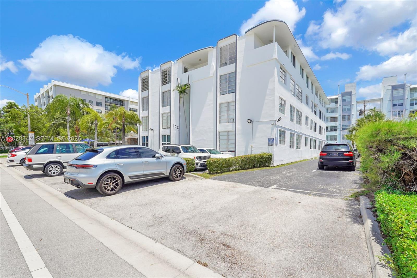A multi-story white apartment building features a parking lot with several cars in front — 1075 93rd St # 207, Bay Harbor Islands FL 33154, BAY HARBOR ISLANDS, FL