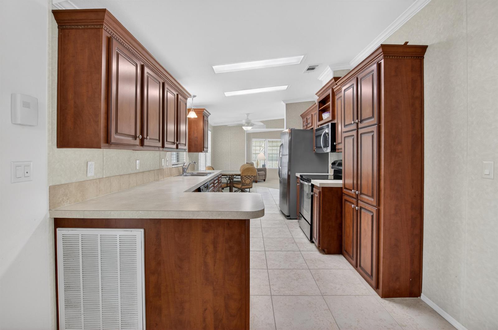 A kitchen features dark wood cabinets, light countertops, stainless steel appliances, and tile flooring — 5006 Curacas Bay, Boynton Beach FL 33436, BOYNTON BEACH, FL