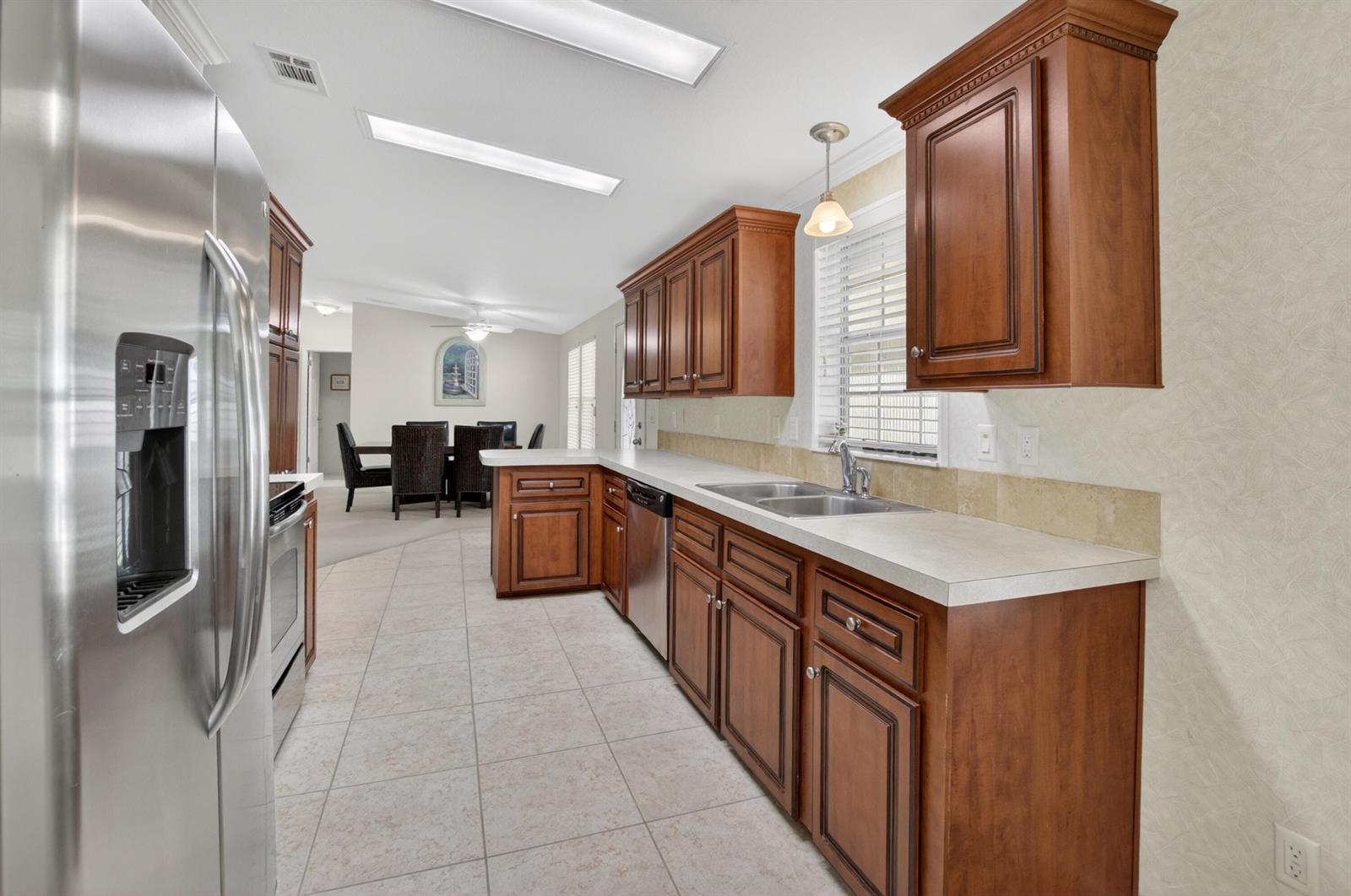 A kitchen features wood cabinets, stainless steel appliances, tile flooring, and a view into the dining area — 5006 Curacas Bay, Boynton Beach FL 33436, BOYNTON BEACH, FL
