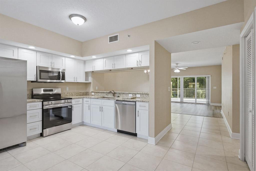 A kitchen with white cabinets, stainless steel appliances, and granite countertops opens to a living area — 960 STARKEY ROAD UNIT 5105, LARGO, FL