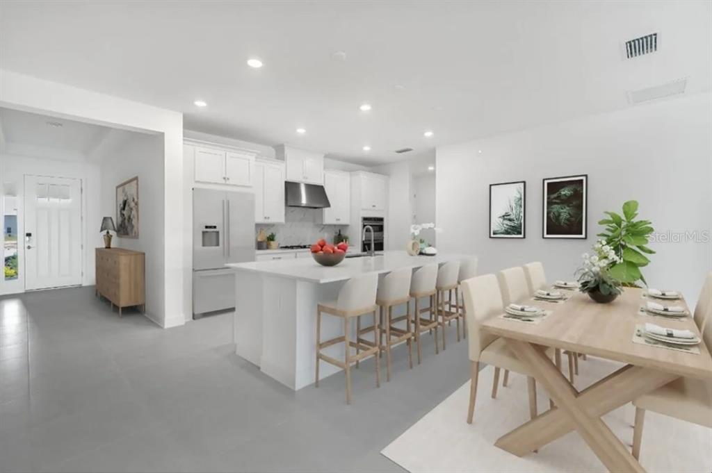 A bright, modern kitchen features white cabinetry, a large island with bar seating, and dining area — 12940 HARVEST RAIN AVENUE, WINTER GARDEN, FL