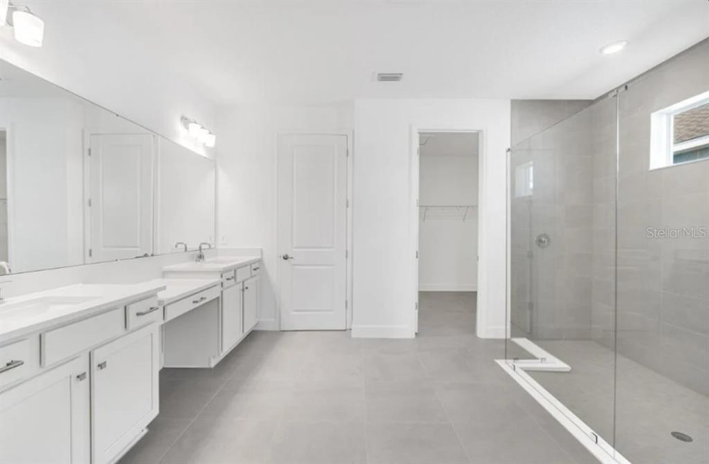 A modern bathroom features a double vanity, a glass-enclosed walk-in shower, and light gray tile — 12940 HARVEST RAIN AVENUE, WINTER GARDEN, FL