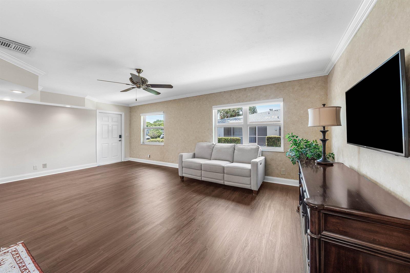 A living room features light-colored walls, wood-look flooring, a sofa, and a wall-mounted television — 2303 Lowson Boulevard # D, Delray Beach FL 33445, DELRAY BEACH, FL