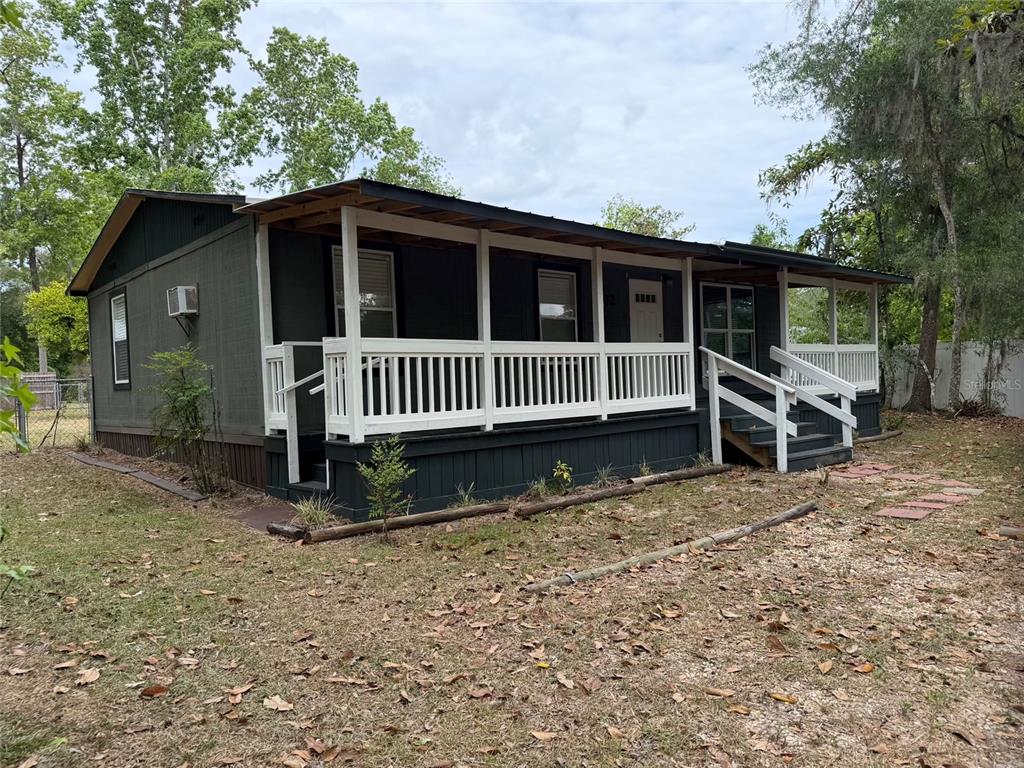 A dark-sided manufactured home features a full-length front porch with white railings and stairs — 8732 CR 647 S, BUSHNELL, FL