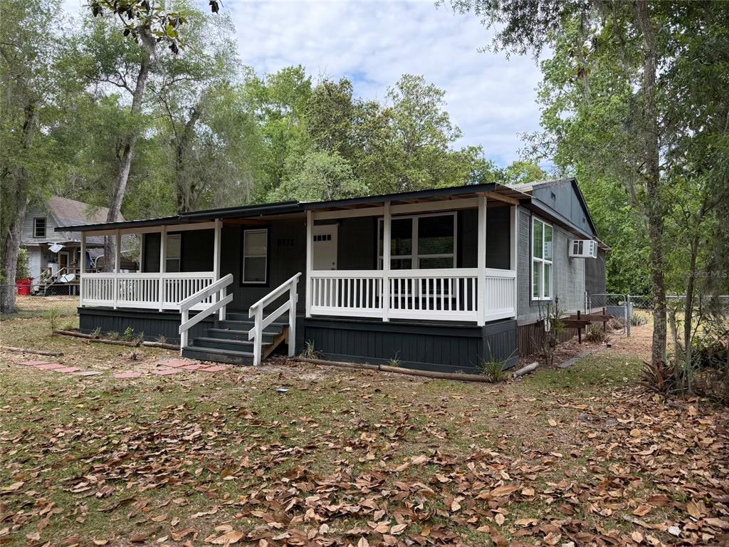 A dark-painted manufactured home features a large white-railed front porch and a metal roof — 8732 CR 647 S, BUSHNELL, FL