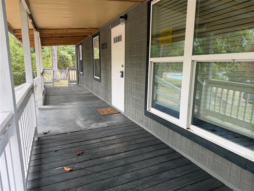 A covered wooden porch leads to a white front door on a gray-sided house — 8732 CR 647 S, BUSHNELL, FL