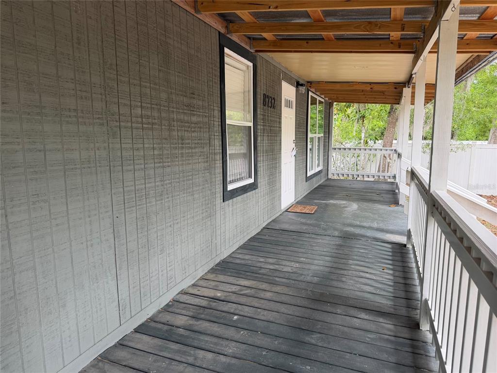 A covered wooden porch features gray vertical siding, a white front door, and railings — 8732 CR 647 S, BUSHNELL, FL